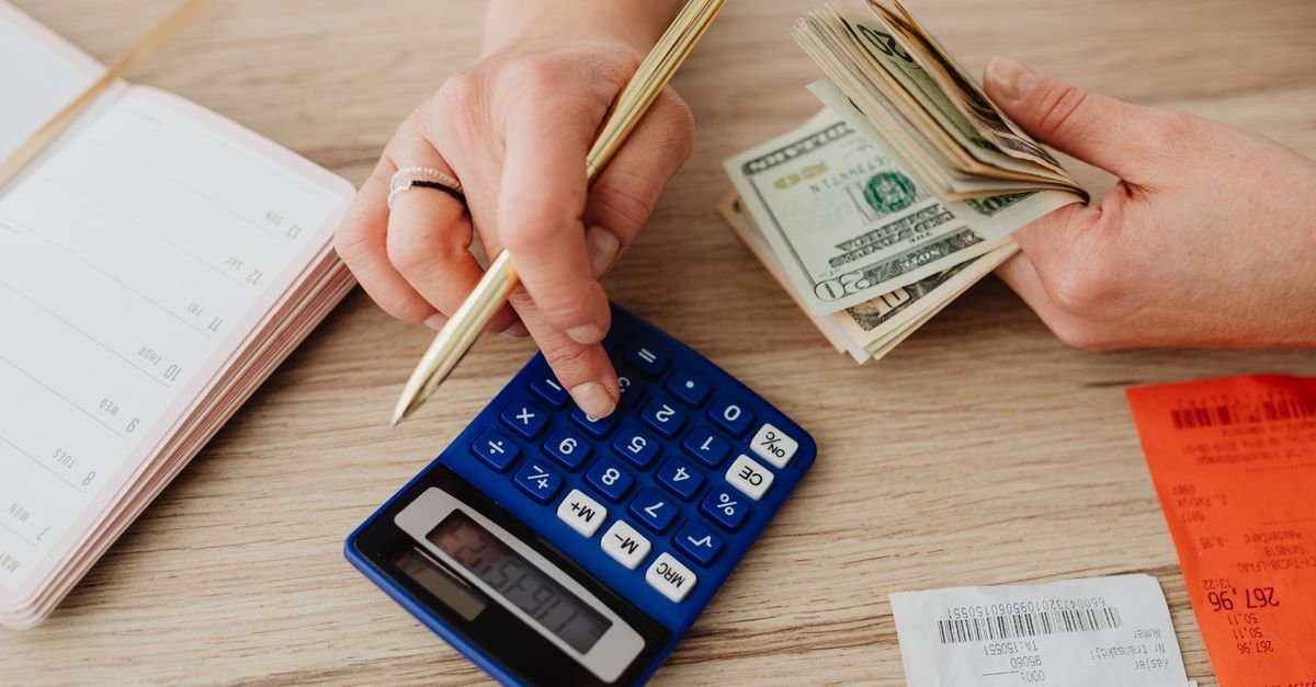 Hands using a calculator beside cash, receipts and an open notebook