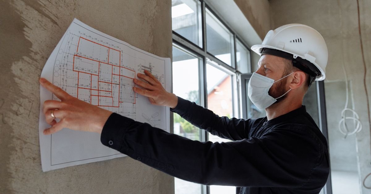 Person in a hard hat pointing at technical drawings on a wall