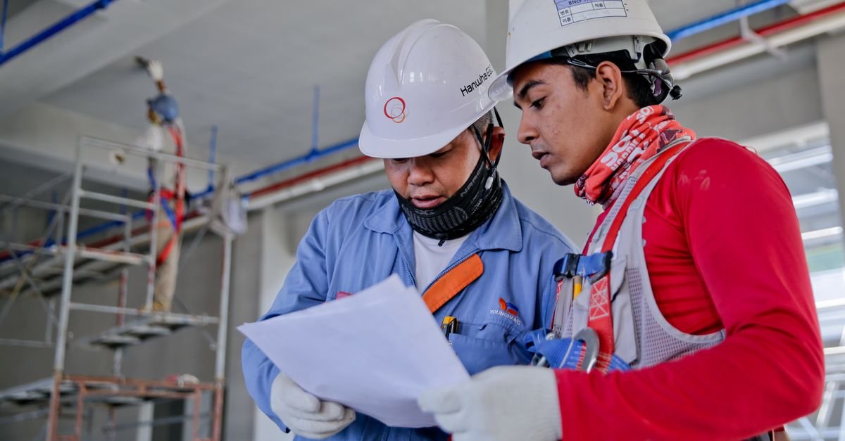 Two construction workers in safety helmets reviewing documents together on a job site