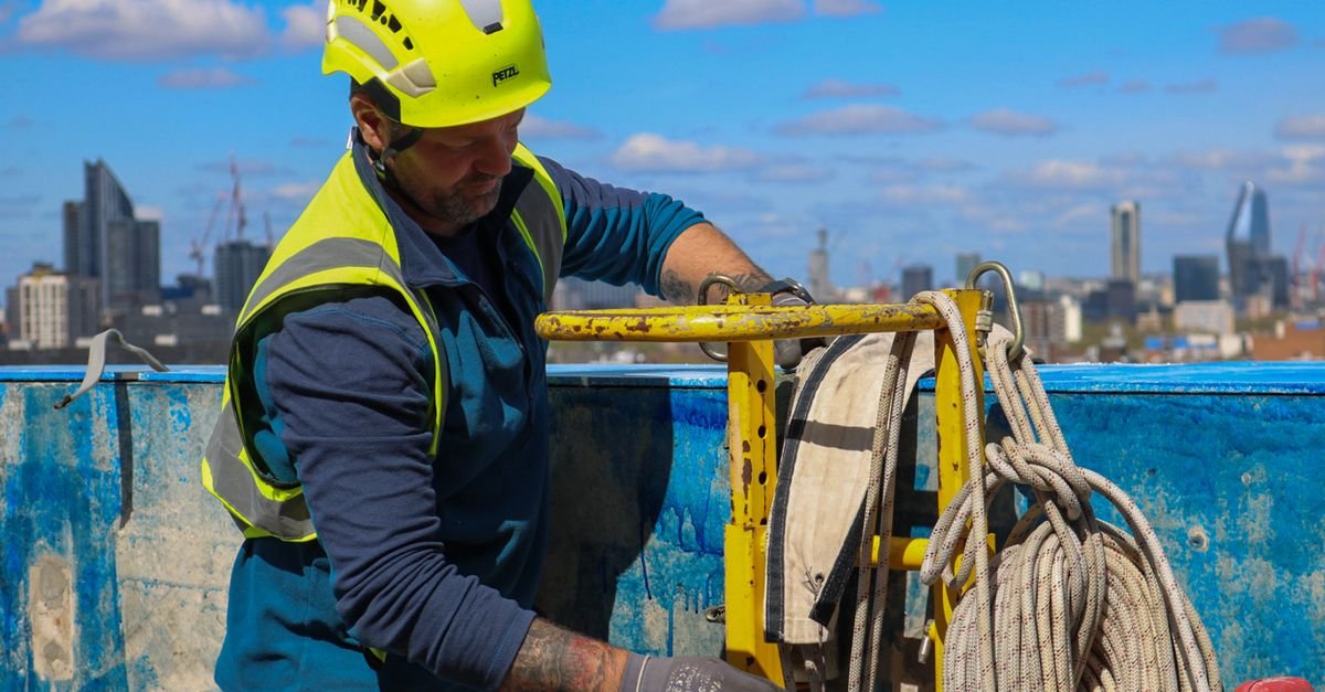 Construction contractor in a hard hat and high visibility jacket working on site equipment