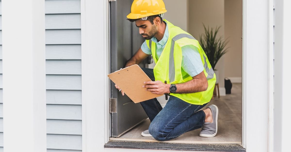 Building inspector in a hard hat and safety vest checking a doorway with a clipboard