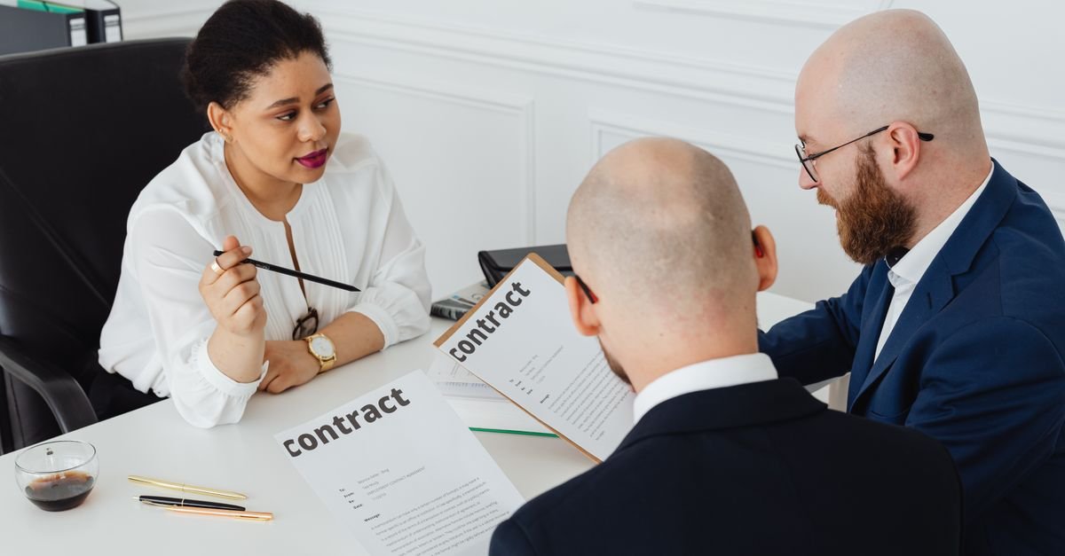 Three people reviewing a construction contract at an office table, the largest NASCLA exam subject area